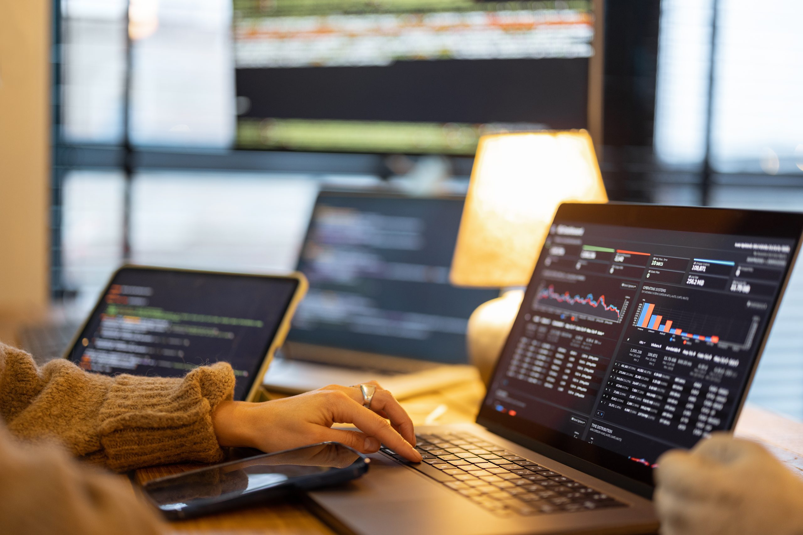 Imagem de uma pessoa usando um laptop com um dashboard em exibição, e no fundo aparecem outras telas de laptop desfocadas